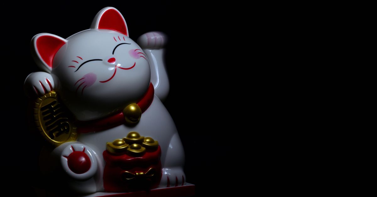 A ceramic Maneki Neko, or lucky cat, figurine symbolizing good fortune, with a dark background.
